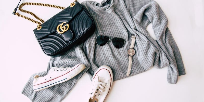Gray sweater, black Gucci bag, and white Converse assembled on the floor